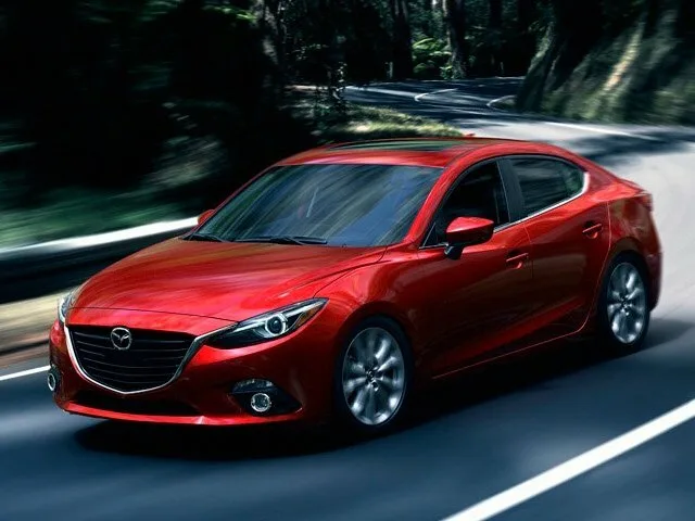 Mazda Axela третьего поколения BM, красный седан в движении по лесной дороге, вид спереди-сбоку слева