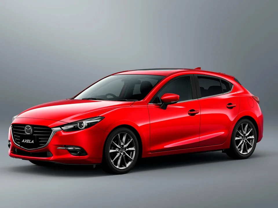 Mazda Axela третьего поколения BM после обновления, красный пятидверный хэтчбек, вид спереди-сбоку слева, серый студийный фон