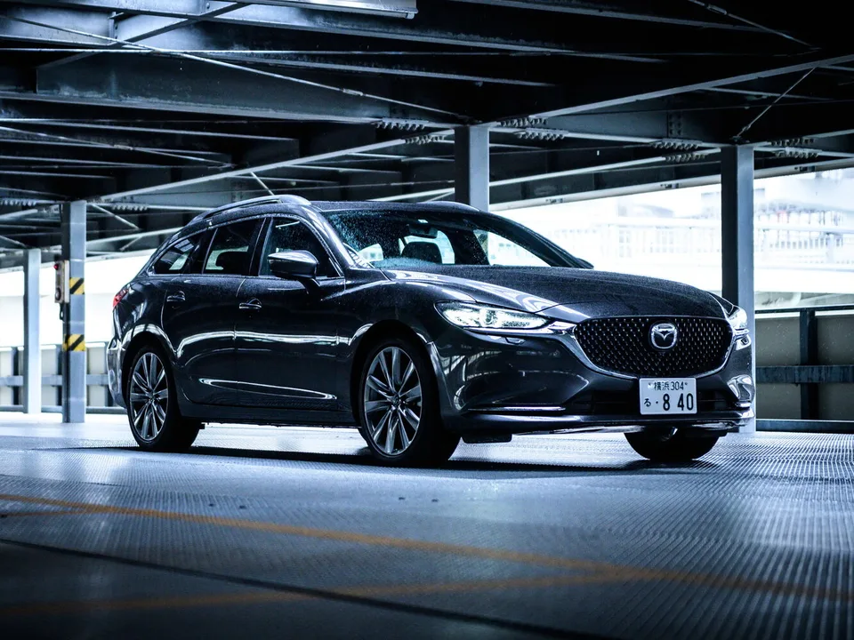 Mazda Atenza последнего периода, тёмный универсал на многоуровневой парковке, вид спереди-сбоку справа, японский номерной знак