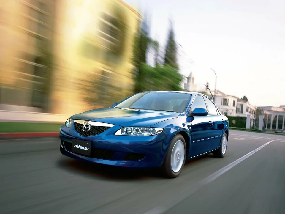 Mazda Atenza первого поколения, синий седан в движении, вид спереди-сбоку слева, на номерном месте табличка Atenza
