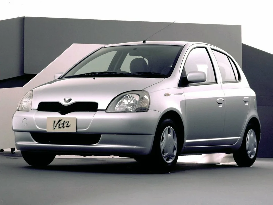 Toyota Vitz первого поколения XP10, серебристый пятидверный хэтчбек, вид спереди-сбоку слева, студийный кадр, на номерном месте надпись Vitz