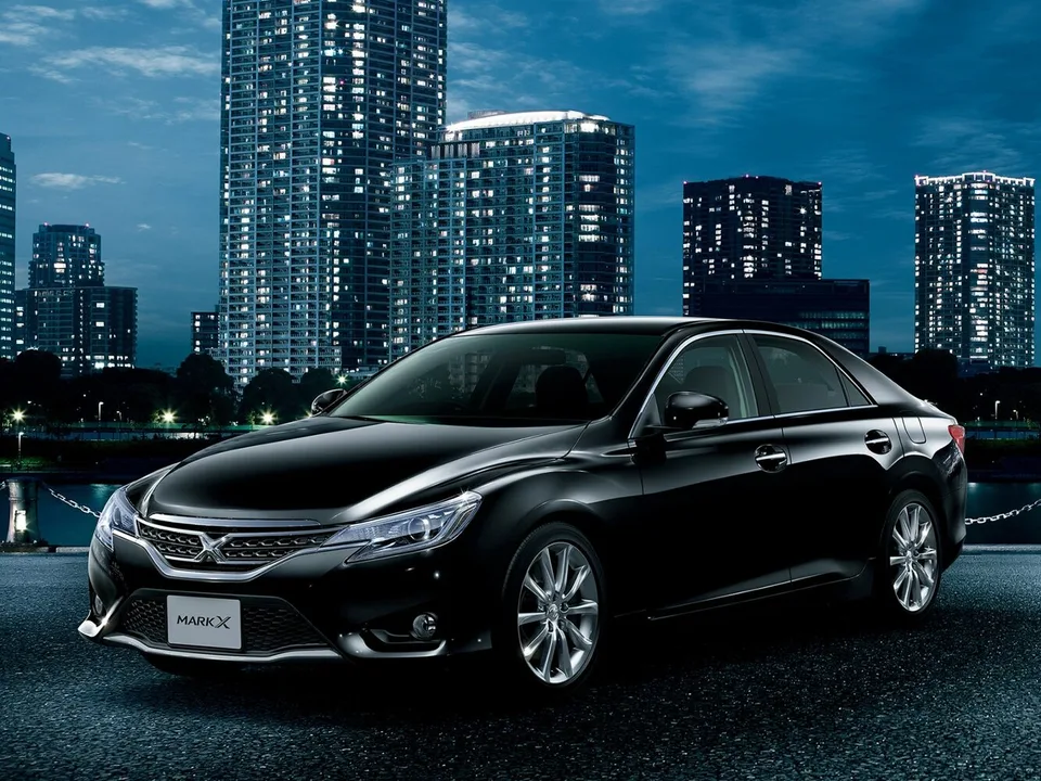 Toyota Mark X второго поколения после обновления 2012 года, чёрный седан на фоне ночного города, широкая хромированная решётка радиатора