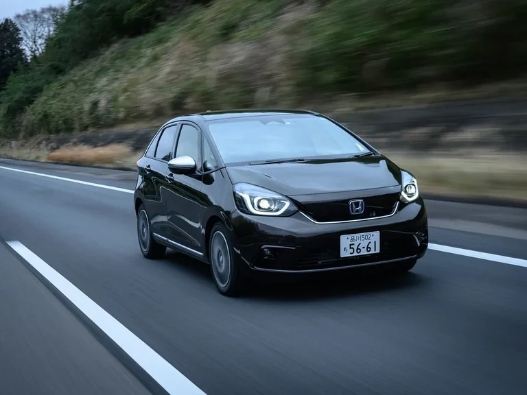 Honda Fit четвёртого поколения GR 2020–2022 годов, гибрид e:HEV, тёмный хэтчбек в движении, вид спереди-сбоку
