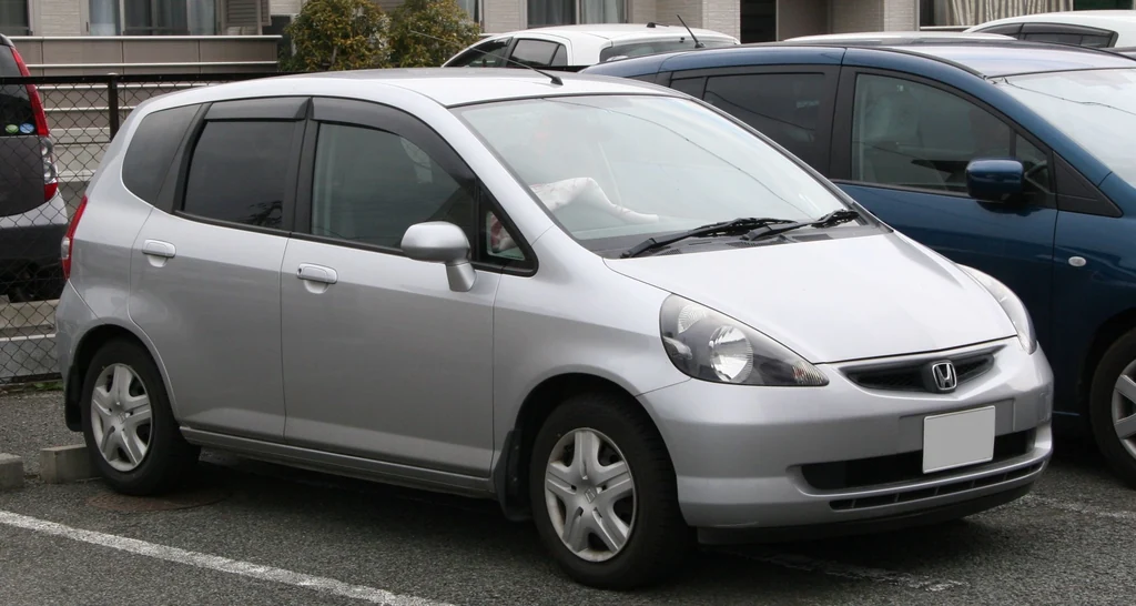 Honda Fit первого поколения GD в исходном облике 2001–2004 годов, серебристый хэтчбек на парковке, вид спереди-сбоку