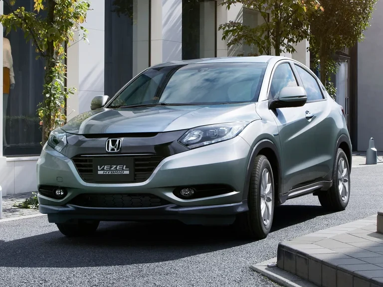 Honda Vezel Hybrid первого поколения RU 2013–2018 годов, серебристый кроссовер у витрины, вид спереди-сбоку