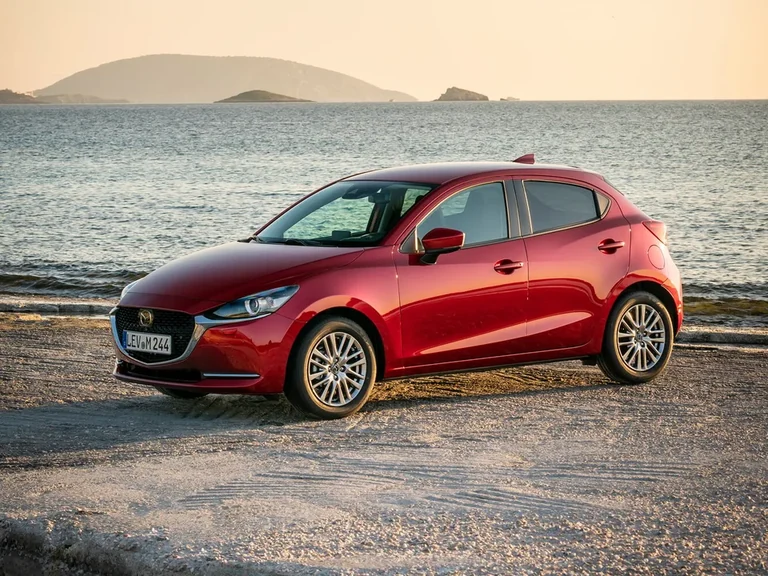 Mazda2 после обновления 2019 года, красный пятидверный хэтчбек с европейским номером на берегу моря