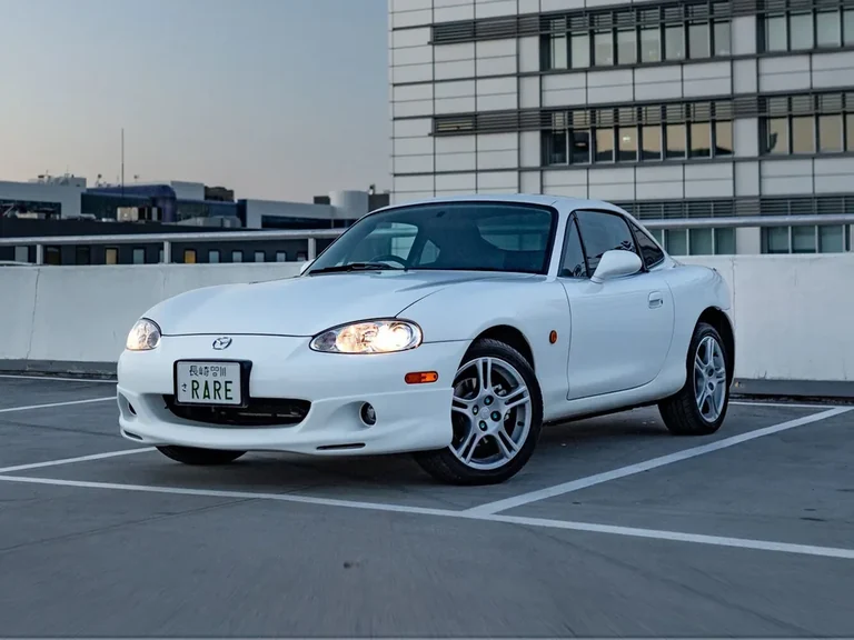 Mazda Roadster Coupe, белое двухместное купе с несъёмной крышей на крыше многоэтажной парковки, вечерний свет
