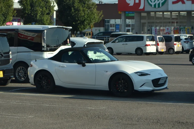Mazda Roadster ND с поднятой мягкой крышей, белый кузов сбоку на японской парковке, чёрные колёса