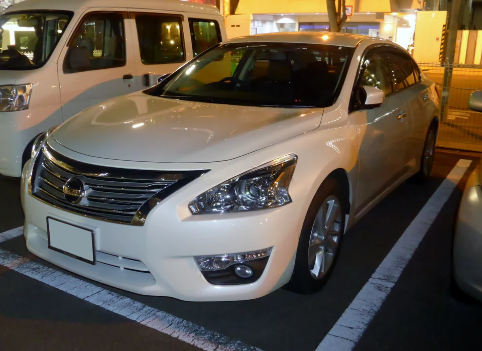 Nissan Teana третьего поколения L33, белый седан на вечерней парковке, вид спереди-сбоку слева, хромированная решётка радиатора