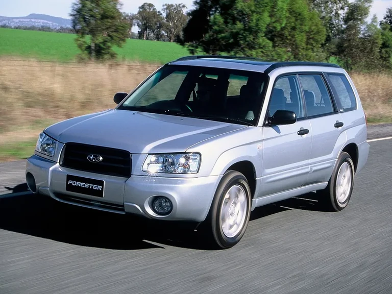 Subaru Forester второго поколения, серебристый кузов в движении по загородной дороге, табличка FORESTER на бампере, водитель справа