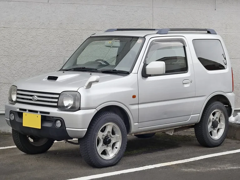 Suzuki Jimny JB23, серебристый трёхдверный внедорожник у стены, воздухозаборник на капоте, узкий кузов без расширителей арок, жёлтый номер