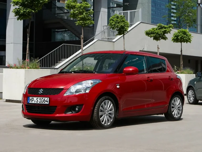 Suzuki Swift поколения 2010–2016 годов, красный пятидверный хэтчбек с европейским номером у здания