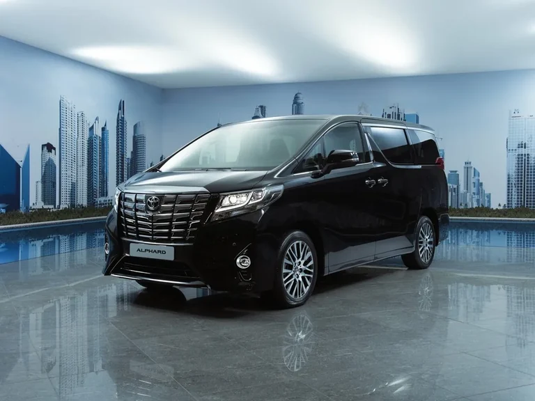 Toyota Alphard третьего поколения до обновления, чёрный минивэн в студии на фоне панорамы небоскрёбов, табличка ALPHARD