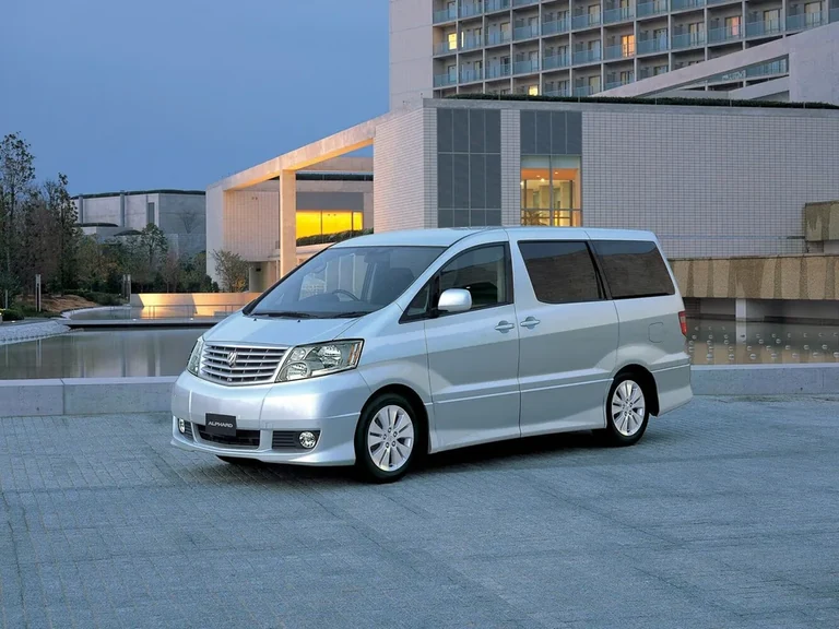Toyota Alphard первого поколения, серебристый минивэн у современного здания, табличка ALPHARD на бампере