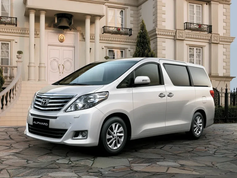 Toyota Alphard второго поколения, белый минивэн перед особняком с колоннами, табличка ALPHARD