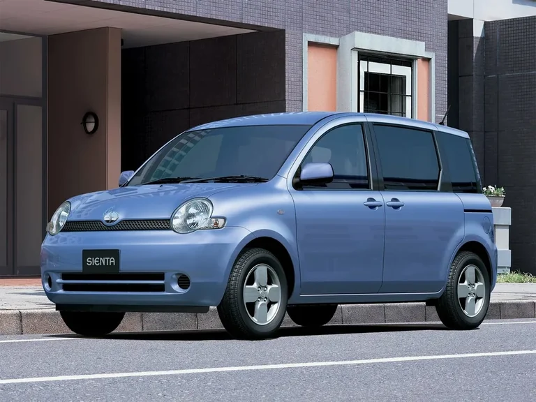 Toyota Sienta первого поколения, синий компактвэн у дома, вид спереди-сбоку