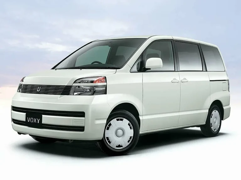 Toyota Voxy первого поколения, белый кузов, вид спереди-сбоку на светлом фоне, табличка VOXY на бампере